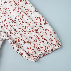 Détail de la manche bouffante élastique avec imprimé floral rouge sur robe blanche