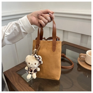 Detail of brown suede crossbody bag featuring a plush leopard print doll charm accessory