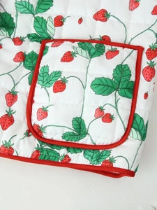 Detail of white quilted fabric jacket with strawberry print and red piped pocket edges