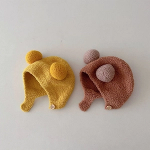 Soft knitted baby earflap hat with double pom-poms and wooden button in yellow and brown
