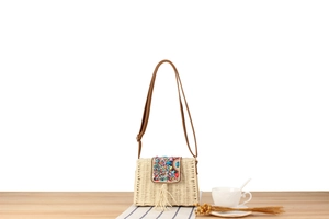 Détail du sac bandoulière en paille avec broderie de perles colorées et glands de coquillages