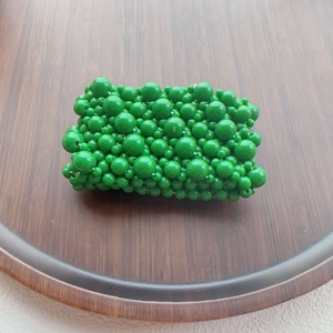 Detailed top view of a handmade green beaded coin purse on a minimalist wooden tray