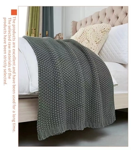 Close-up of thick grey cable knit throw blanket with fringe on a white cozy bed