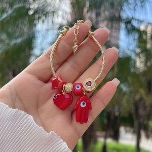 Detailed shot of 18K gold Hamsa Hand and red Evil Eye charms on adjustable chain