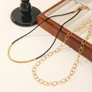 Detail of beaded black spinel necklace and gold oval link chain on wooden tray