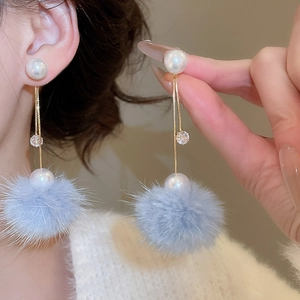Detail of 18K gold plated drop earrings with blue faux fur pom-poms and pearls on model