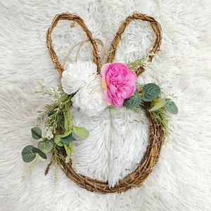 Close-up of woven rattan Easter bunny wreath with pink flowers on white plush background