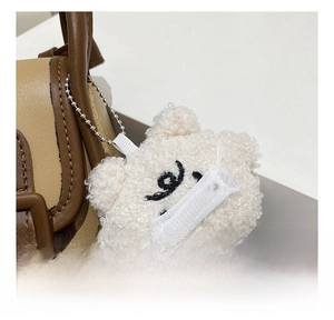 Detailed close-up of a white plush bear charm with silver ball chain on a brown bag
