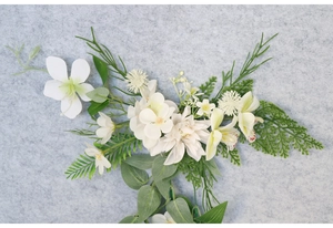 Detailed view of handmade bridal hairpiece with white faux flowers and green eucalyptus leaves