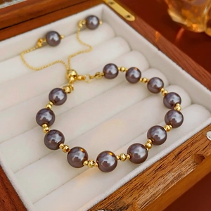 Detail of adjustable pearl bracelet with grey pearls and gold toggle on white velvet