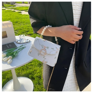 Detail of white floral embroidery bag with pearl handle and golden buckle on grass
