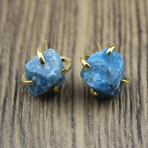 Macro shot of natural raw blue stones secured in golden four-prong stud earrings