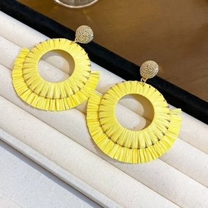 Detail view of yellow raffia fringe earrings with golden textured ball stud on a white stand