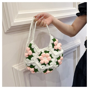 Close-up of handmade white crochet crescent bag featuring pink flowers and green leaves