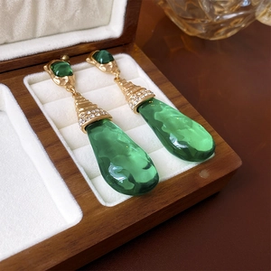Macro detail of vintage gold earrings with green water-drop gems in a luxury box