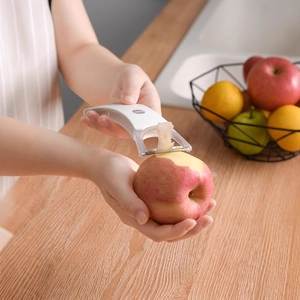 White kitchen fruit peeler peeling a red apple on a clean wooden countertop