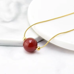Titanium steel snake chain necklace with a red agate bead and gold accents on marble