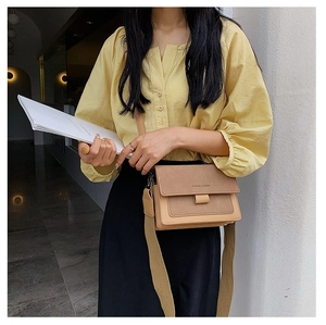 Detail of khaki crossbody bag with wide fabric strap and suede texture shown on a model