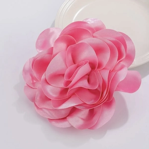 Close-up of pink satin flower brooch with layered petals on a minimalist white surface