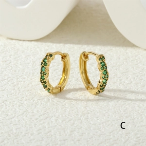 Detailed macro view of gold huggie earrings featuring double rows of green zircon stones