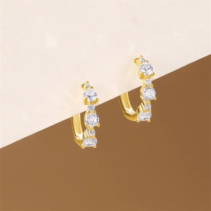 Close-up of gold-plated geometric hoop earrings featuring sparkling white zircon stones