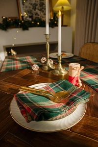 Close-up of festive red and green plaid napkins with elegant gold cutlery and white plates