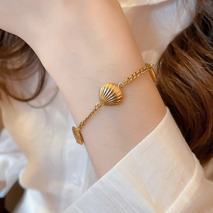 Detail of golden stainless steel bracelet featuring multiple textured seashell pendants