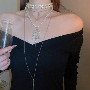Detail of layered silver necklaces with pearls and crystal cross pendants on model