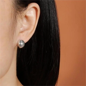 Macro shot of a silver spherical earring with textured threads worn by a model