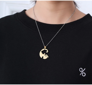 Detail showing a gold-toned cat pendant on a fine silver chain worn over a black sweater