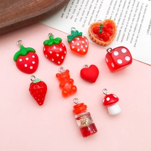 Detailed view of red resin fruit and heart charms for DIY jewelry making on pink background