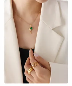 Close-up of golden molten heart necklace with green zircon and rings on a white blazer