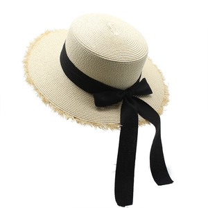 Close-up of woven raffia boater hat detailing fringe edges and black ribbon bow decoration