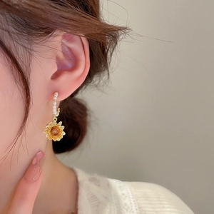 Close-up of a gold sunflower earring with pearls worn by a model for a stylish look