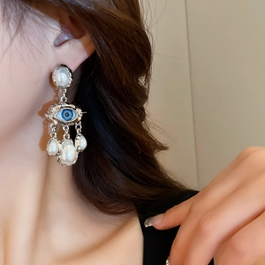 Close-up of retro eye earrings with white pearls and blue eye element on model