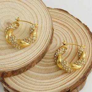 Detail view of gold twisted hoop earrings with crystals on natural wood background