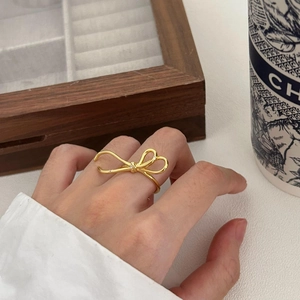 Detail of a minimalist gold bow ring with small zircon stones on a wooden tray