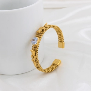 Detail of gold mesh bangle featuring a heart-shaped gem and delicate floral engraving