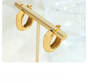 Détail macro de boucles d'oreilles C dorées avec fini poli et texture rayée interne