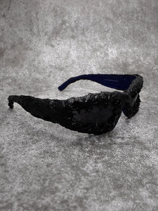 Detail view of matte black avant-garde sunglasses with lava texture and silver temple branding