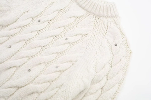Nahaufnahme cremefarbener Zopfstrickpullover mit glitzernden Strasssteinen und Rundhalsausschnitt