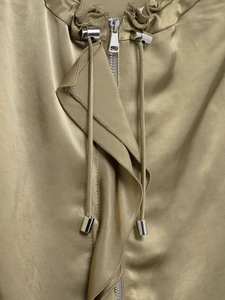 Detailed close-up of khaki satin jacket featuring metallic zipper and drawstring neck