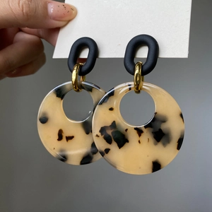 Detail of beige tortoiseshell resin earrings with black oval stud and gold connector