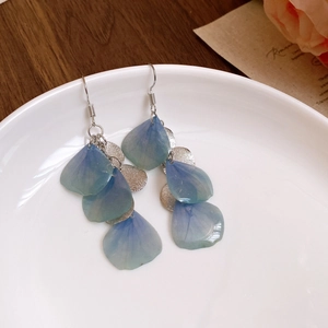 Detailed close-up of blue resin flower petal earrings with silver sequin accents on ceramic