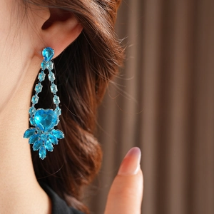 Detail of luxury heart earring with blue zircon gemstones worn on a model's ear