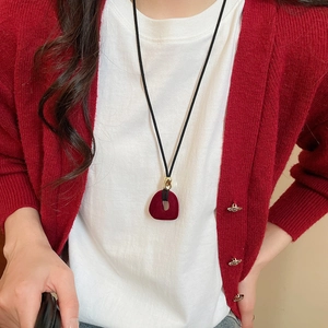 Detail of red flocked resin pendant on a black cord necklace worn with a white t-shirt