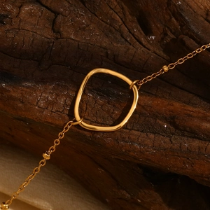 Dettaglio di un ciondolo geometrico quadrato placcato oro 18K su uno sfondo di legno rustico
