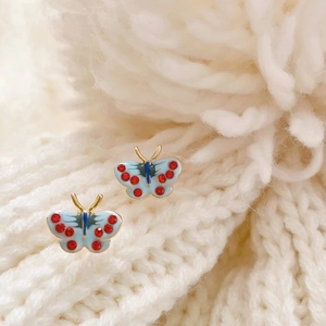 Close-up of S925 blue butterfly stud earrings with red crystals on a soft knitted texture