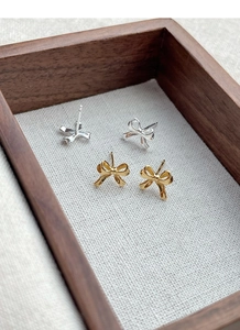 Detail shot of gold and silver bow stud earrings presented in a premium wooden gift box