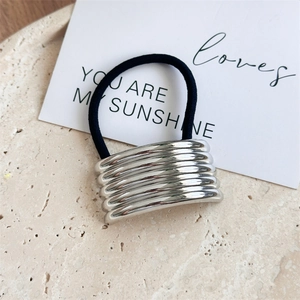 Close-up of a silver wavy metal hair tie on a beige stone surface with minimalist decor